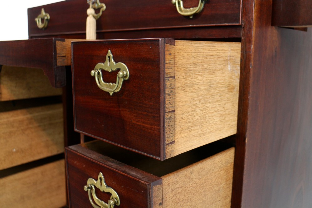 An antique George II red walnut kneehole desk featuring a hinged top that opens to reveal internal compartments and an adjustable green leather mirror, resting on bracket feet with brass handles. View XXV
