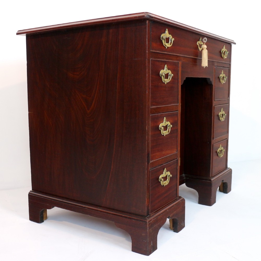 An antique George II red walnut kneehole desk featuring a hinged top that opens to reveal internal compartments and an adjustable green leather mirror, resting on bracket feet with brass handles. View XXVI