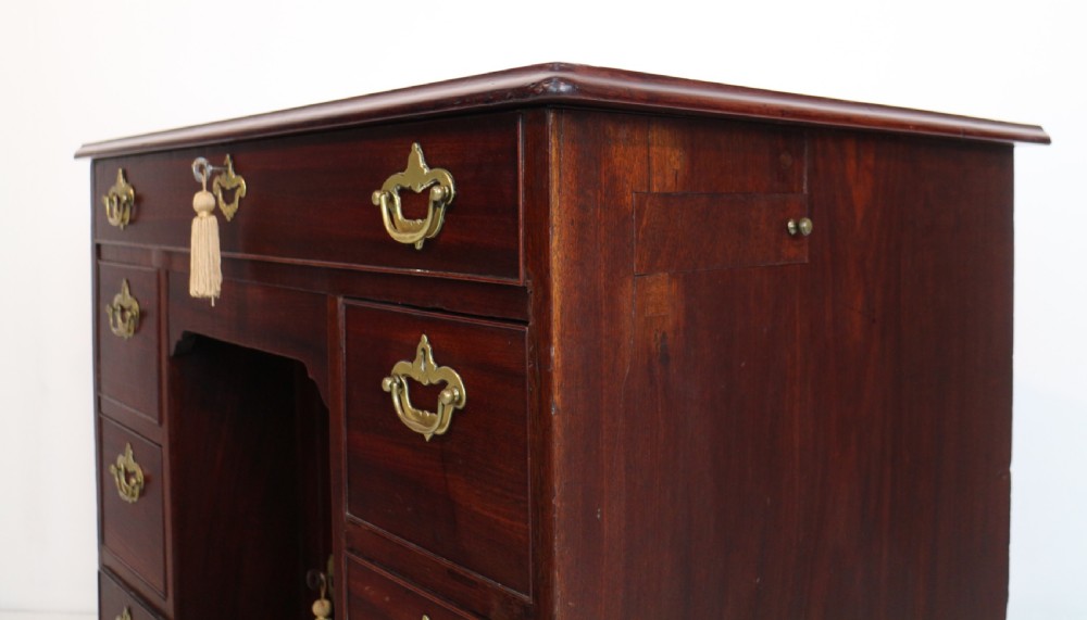 An antique George II red walnut kneehole desk featuring a hinged top that opens to reveal internal compartments and an adjustable green leather mirror, resting on bracket feet with brass handles. View XXVII