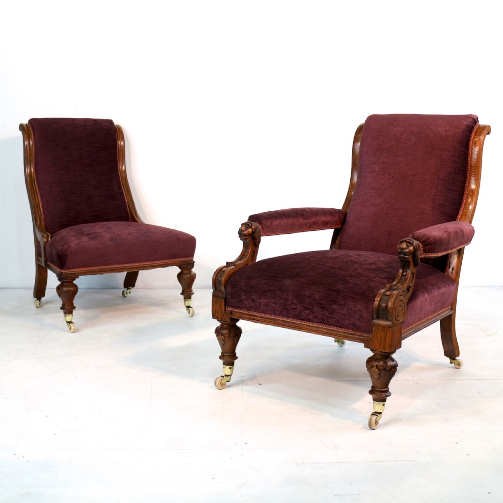 A pair of Victorian oak library chairs upholstered in plum velvet featuring carved lion head arm terminals and brass castors.