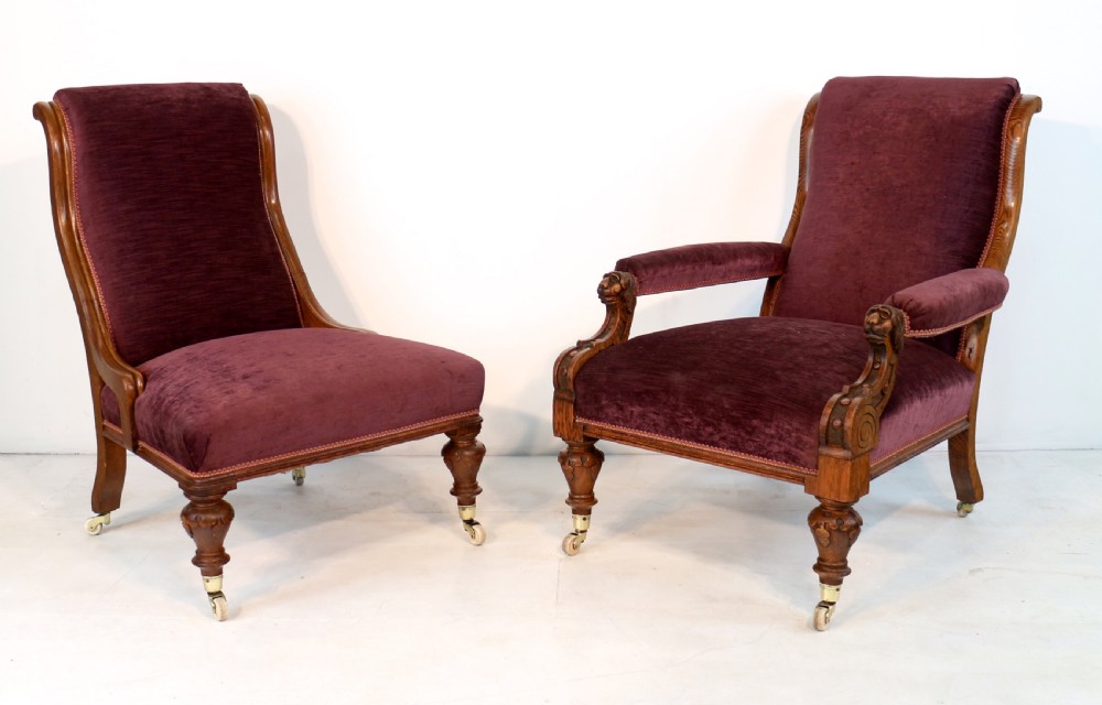 A pair of Victorian oak library chairs upholstered in plum velvet featuring carved lion head arm terminals and brass castors. View II