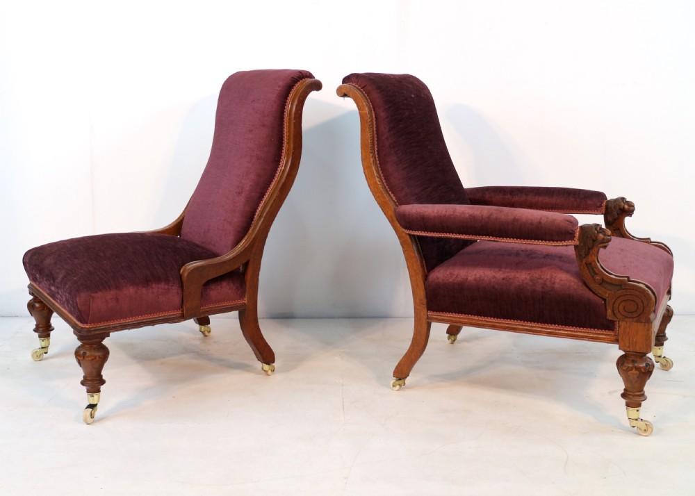A pair of Victorian oak library chairs upholstered in plum velvet featuring carved lion head arm terminals and brass castors. View V