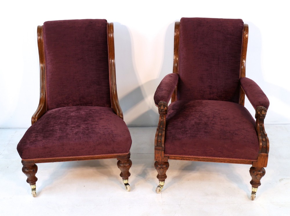 A pair of Victorian oak library chairs upholstered in plum velvet featuring carved lion head arm terminals and brass castors. View VI