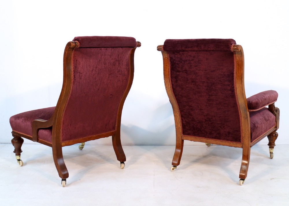 A pair of Victorian oak library chairs upholstered in plum velvet featuring carved lion head arm terminals and brass castors. View VII