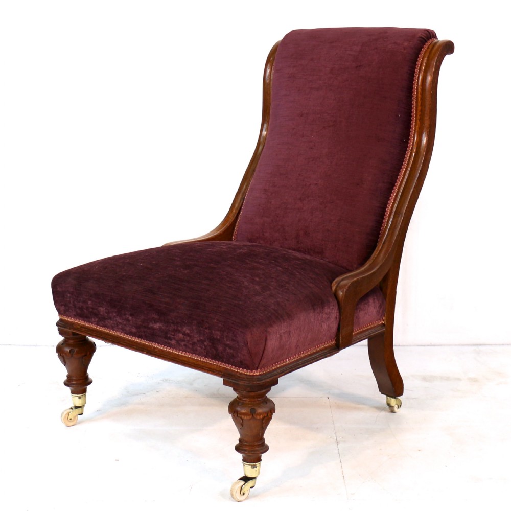 A pair of Victorian oak library chairs upholstered in plum velvet featuring carved lion head arm terminals and brass castors. View VIII