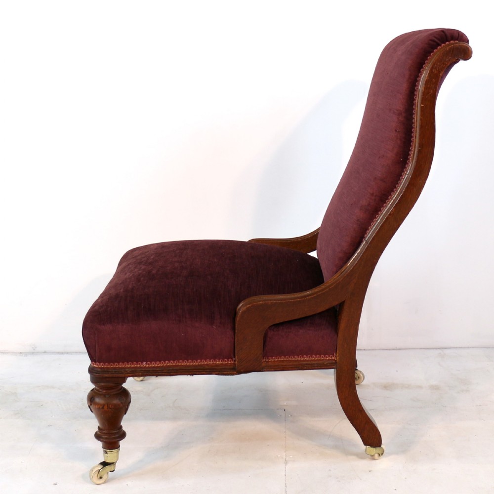A pair of Victorian oak library chairs upholstered in plum velvet featuring carved lion head arm terminals and brass castors. View IX