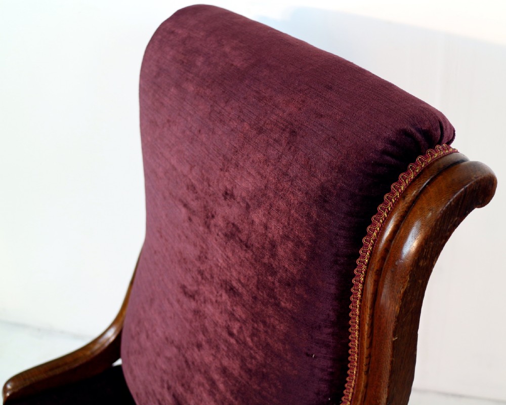 A pair of Victorian oak library chairs upholstered in plum velvet featuring carved lion head arm terminals and brass castors. View X
