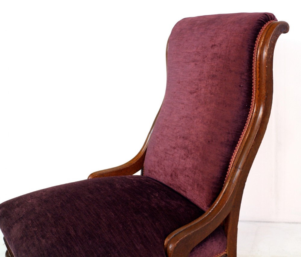 A pair of Victorian oak library chairs upholstered in plum velvet featuring carved lion head arm terminals and brass castors. View XI