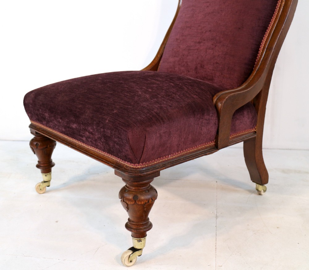 A pair of Victorian oak library chairs upholstered in plum velvet featuring carved lion head arm terminals and brass castors. View XII
