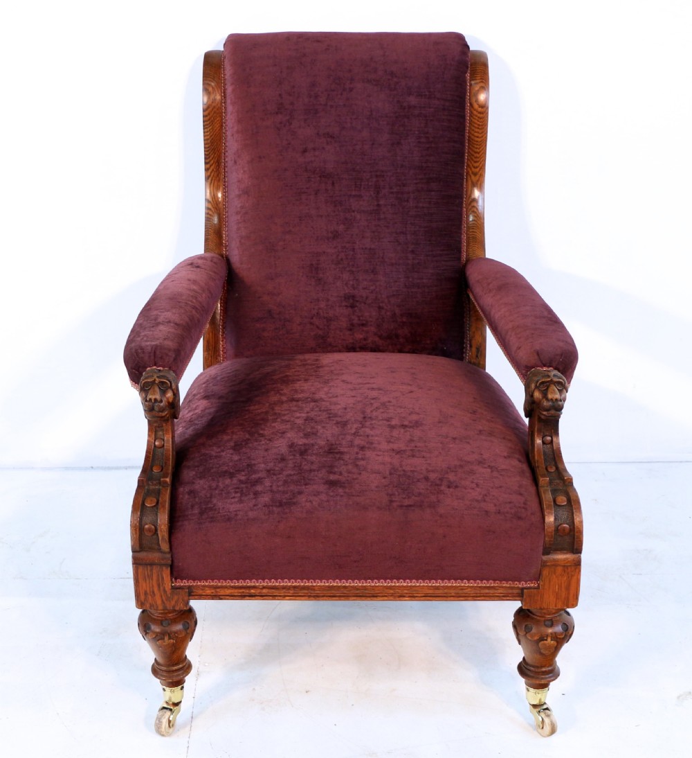 A pair of Victorian oak library chairs upholstered in plum velvet featuring carved lion head arm terminals and brass castors. View XVI