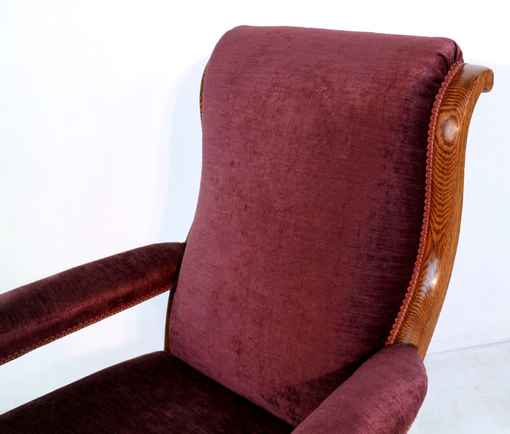 A pair of Victorian oak library chairs upholstered in plum velvet featuring carved lion head arm terminals and brass castors. View XVII