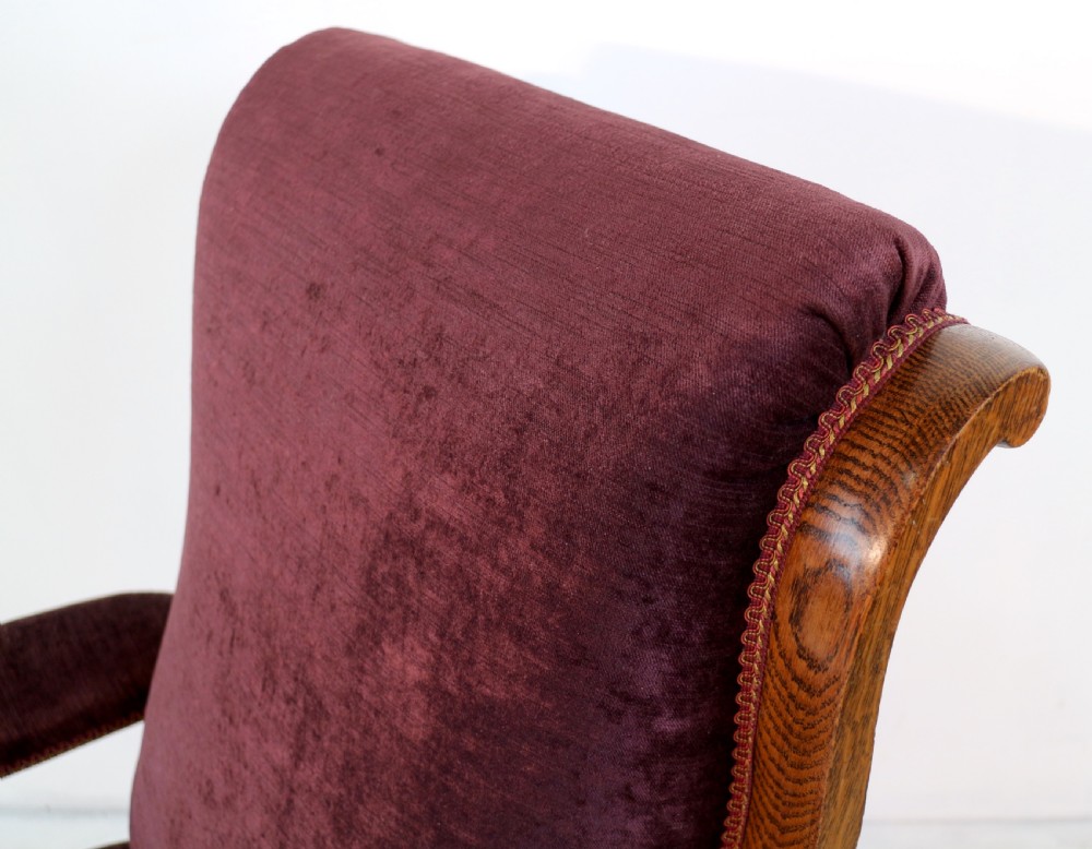 A pair of Victorian oak library chairs upholstered in plum velvet featuring carved lion head arm terminals and brass castors. View XVIII