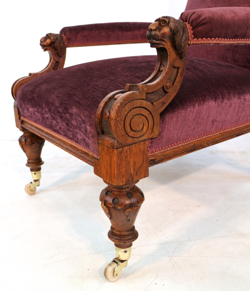 A pair of Victorian oak library chairs upholstered in plum velvet featuring carved lion head arm terminals and brass castors. View XIX