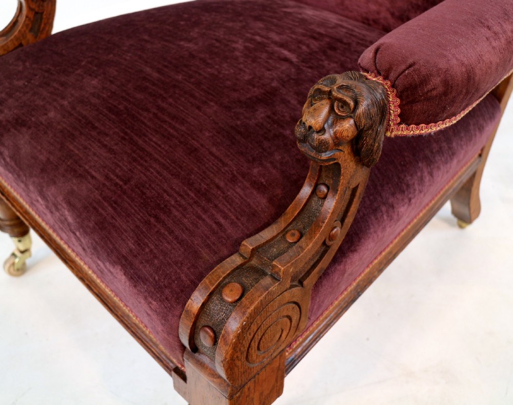 A pair of Victorian oak library chairs upholstered in plum velvet featuring carved lion head arm terminals and brass castors. View XX