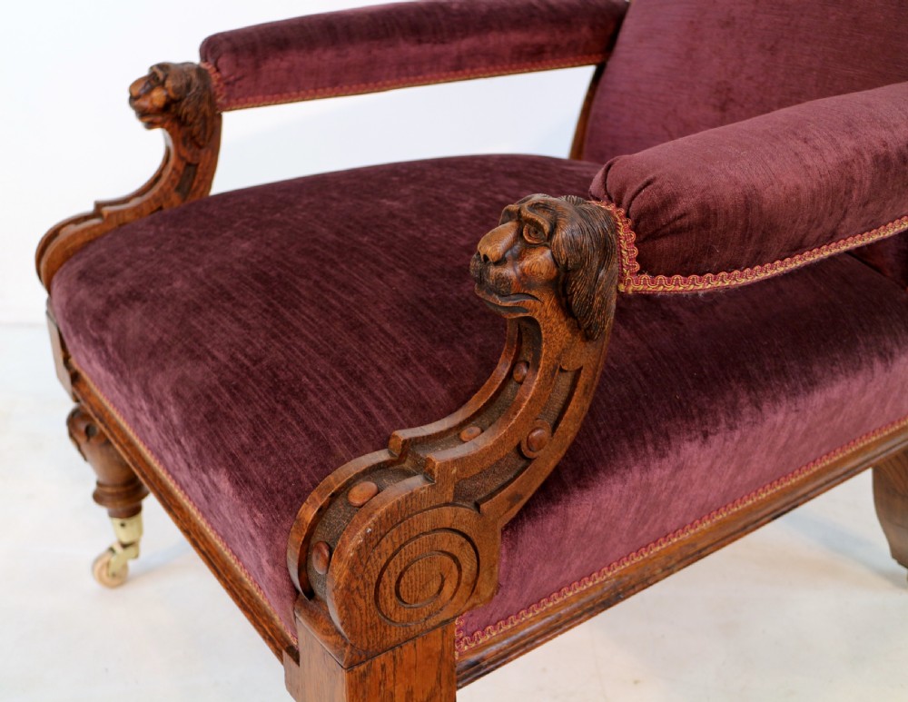 A pair of Victorian oak library chairs upholstered in plum velvet featuring carved lion head arm terminals and brass castors. View XXI