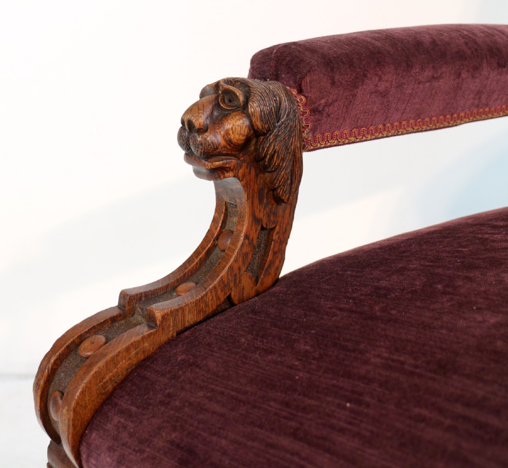 A pair of Victorian oak library chairs upholstered in plum velvet featuring carved lion head arm terminals and brass castors. View XXII