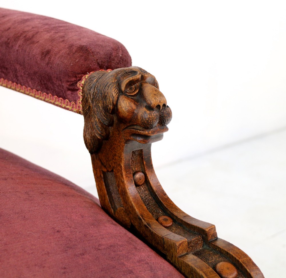 A pair of Victorian oak library chairs upholstered in plum velvet featuring carved lion head arm terminals and brass castors. View XXIII