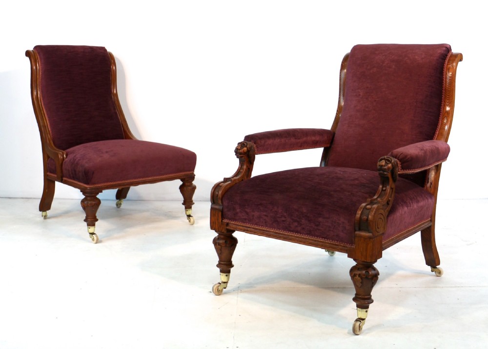 A pair of Victorian oak library chairs upholstered in plum velvet featuring carved lion head arm terminals and brass castors. View XXVII