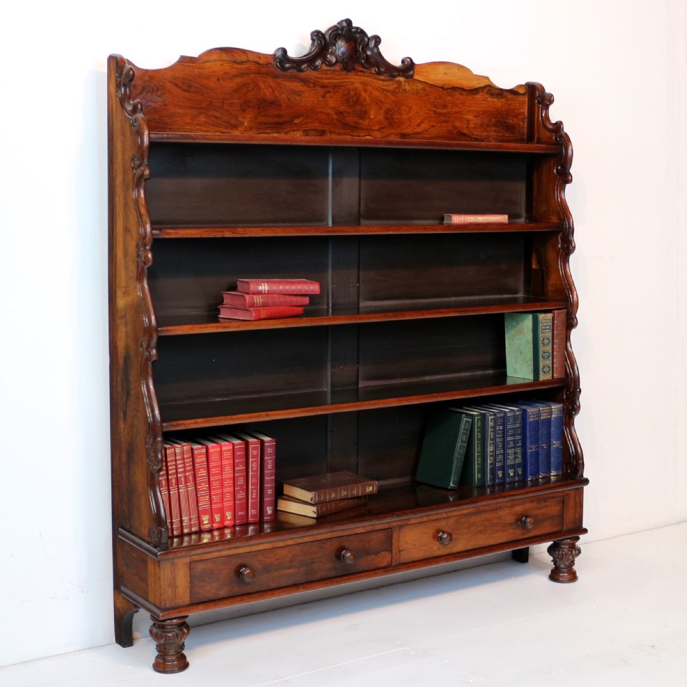A Regency period rosewood waterfall bookcase with graduated open shelves, carved scroll sides, lower drawers, and turned feet.
