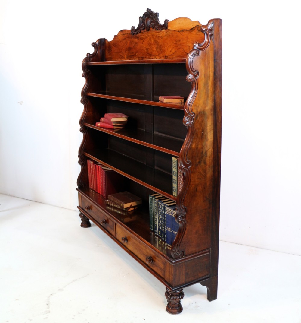 A Regency period rosewood waterfall bookcase with graduated open shelves, carved scroll sides, lower drawers, and turned feet. View II