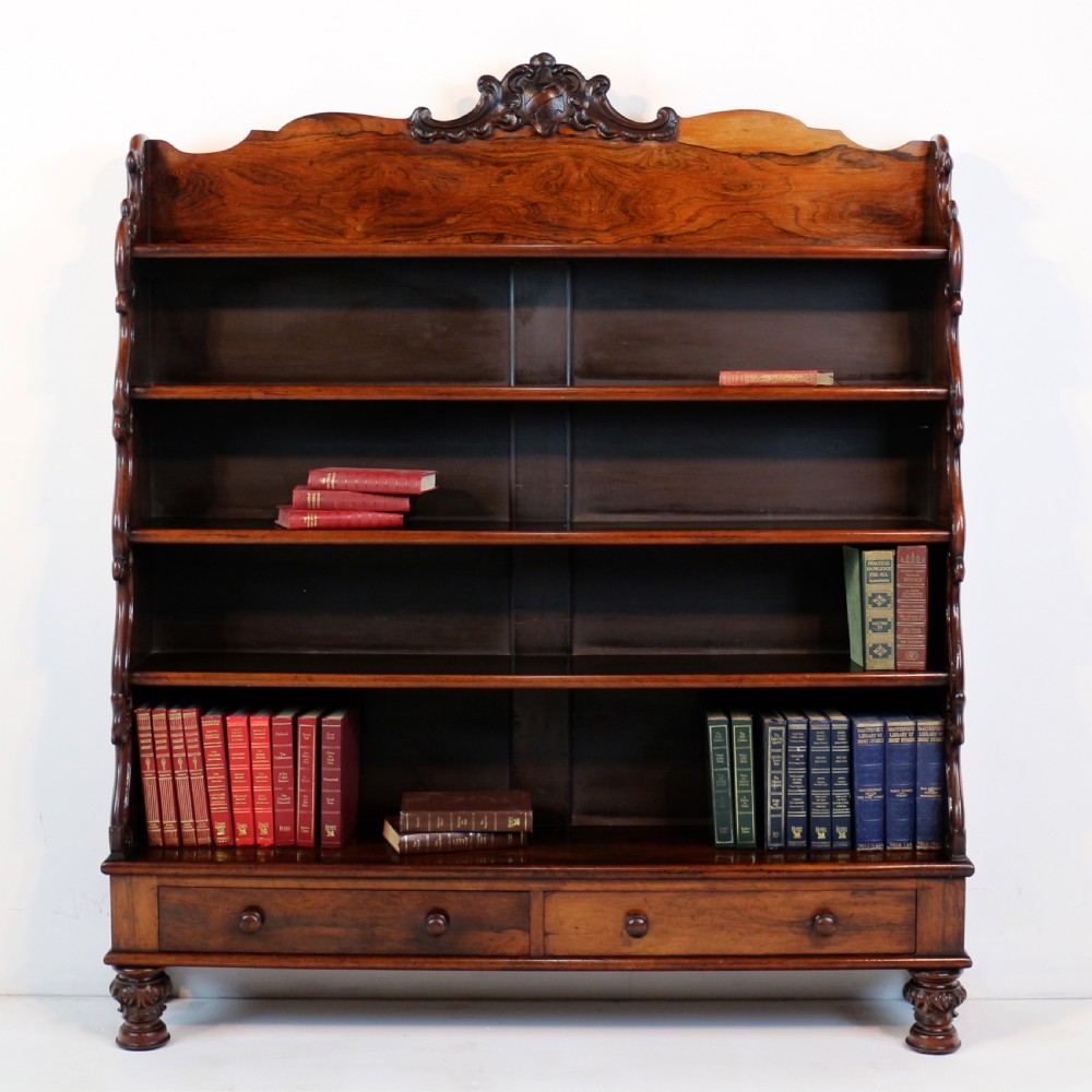 A Regency period rosewood waterfall bookcase with graduated open shelves, carved scroll sides, lower drawers, and turned feet. View IV