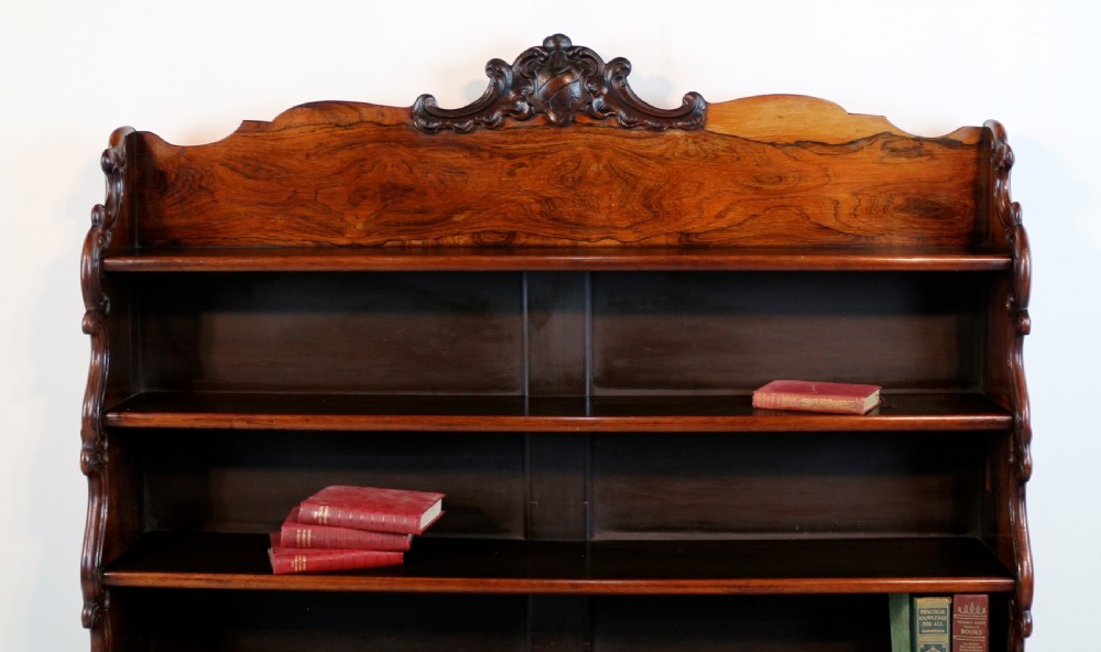 A Regency period rosewood waterfall bookcase with graduated open shelves, carved scroll sides, lower drawers, and turned feet. View VI