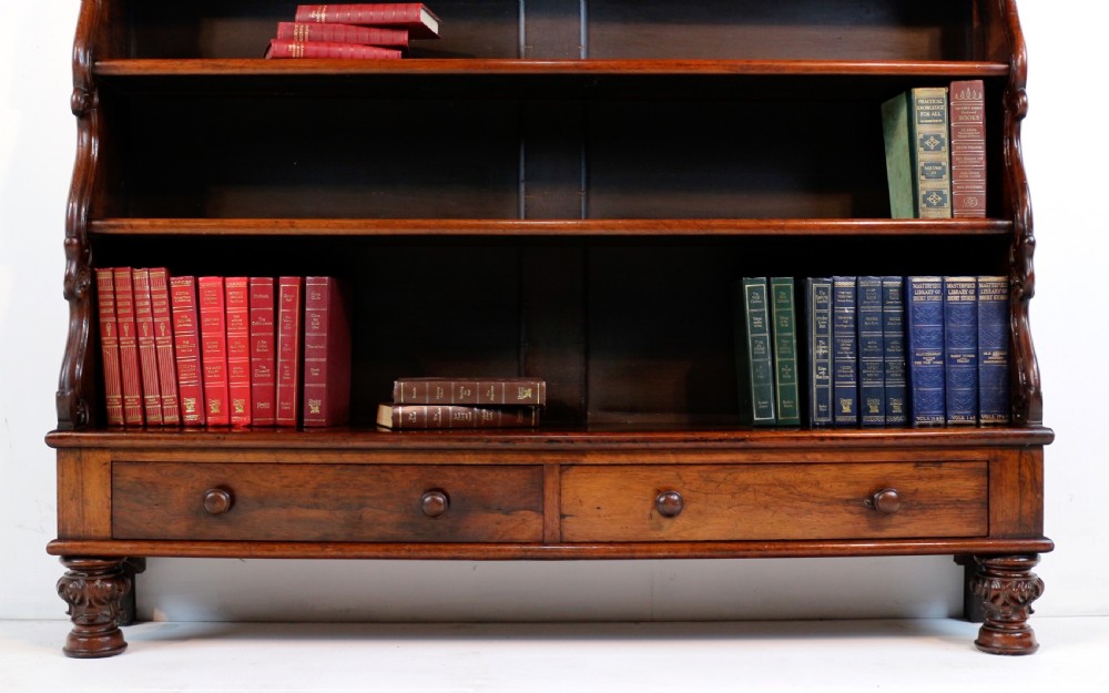 A Regency period rosewood waterfall bookcase with graduated open shelves, carved scroll sides, lower drawers, and turned feet. View VIII