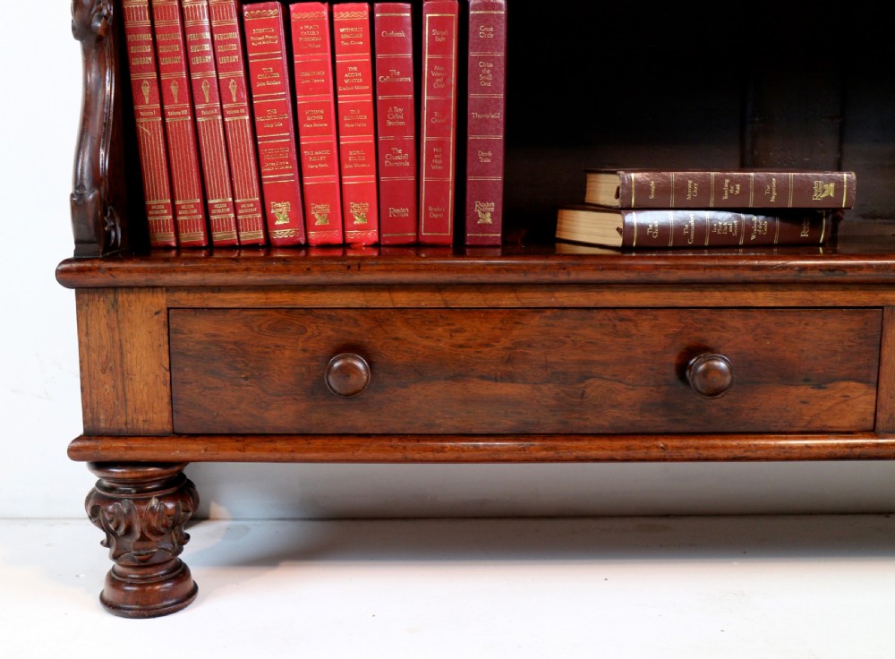 A Regency period rosewood waterfall bookcase with graduated open shelves, carved scroll sides, lower drawers, and turned feet. View IX