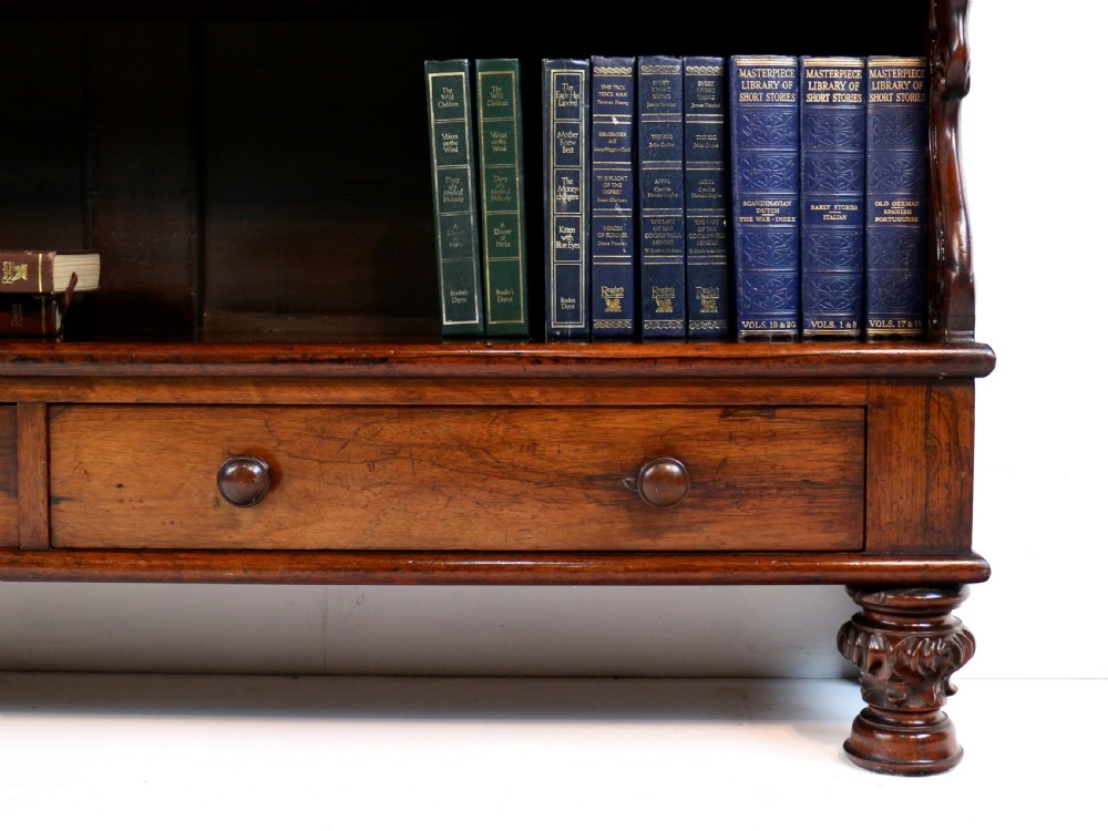 A Regency period rosewood waterfall bookcase with graduated open shelves, carved scroll sides, lower drawers, and turned feet. View X