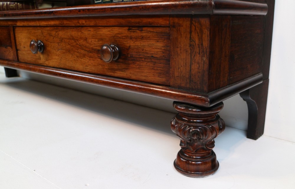 A Regency period rosewood waterfall bookcase with graduated open shelves, carved scroll sides, lower drawers, and turned feet. View XI