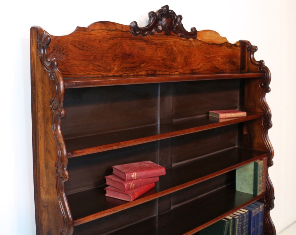 A Regency period rosewood waterfall bookcase with graduated open shelves, carved scroll sides, lower drawers, and turned feet. View XII