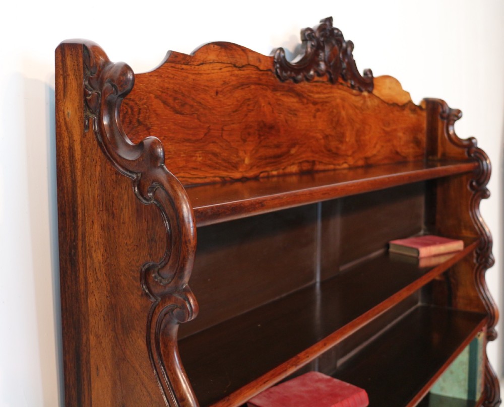 A Regency period rosewood waterfall bookcase with graduated open shelves, carved scroll sides, lower drawers, and turned feet. View XIII