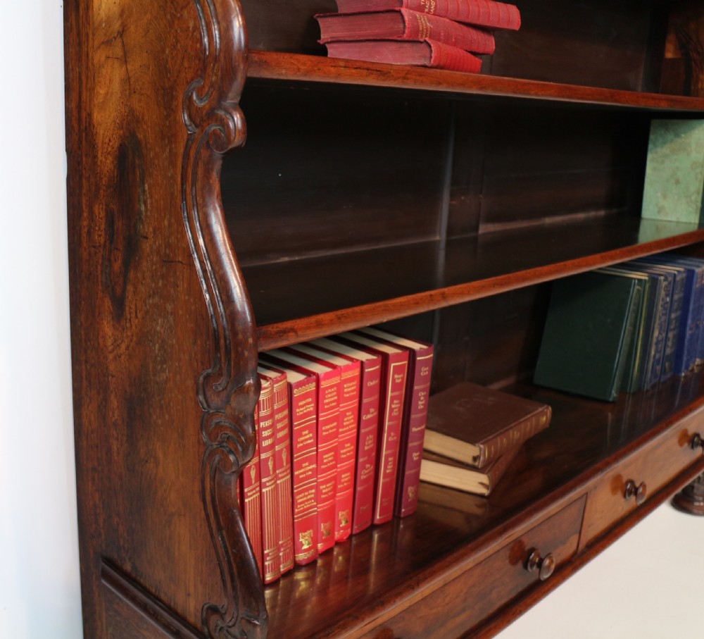 A Regency period rosewood waterfall bookcase with graduated open shelves, carved scroll sides, lower drawers, and turned feet. View XIV