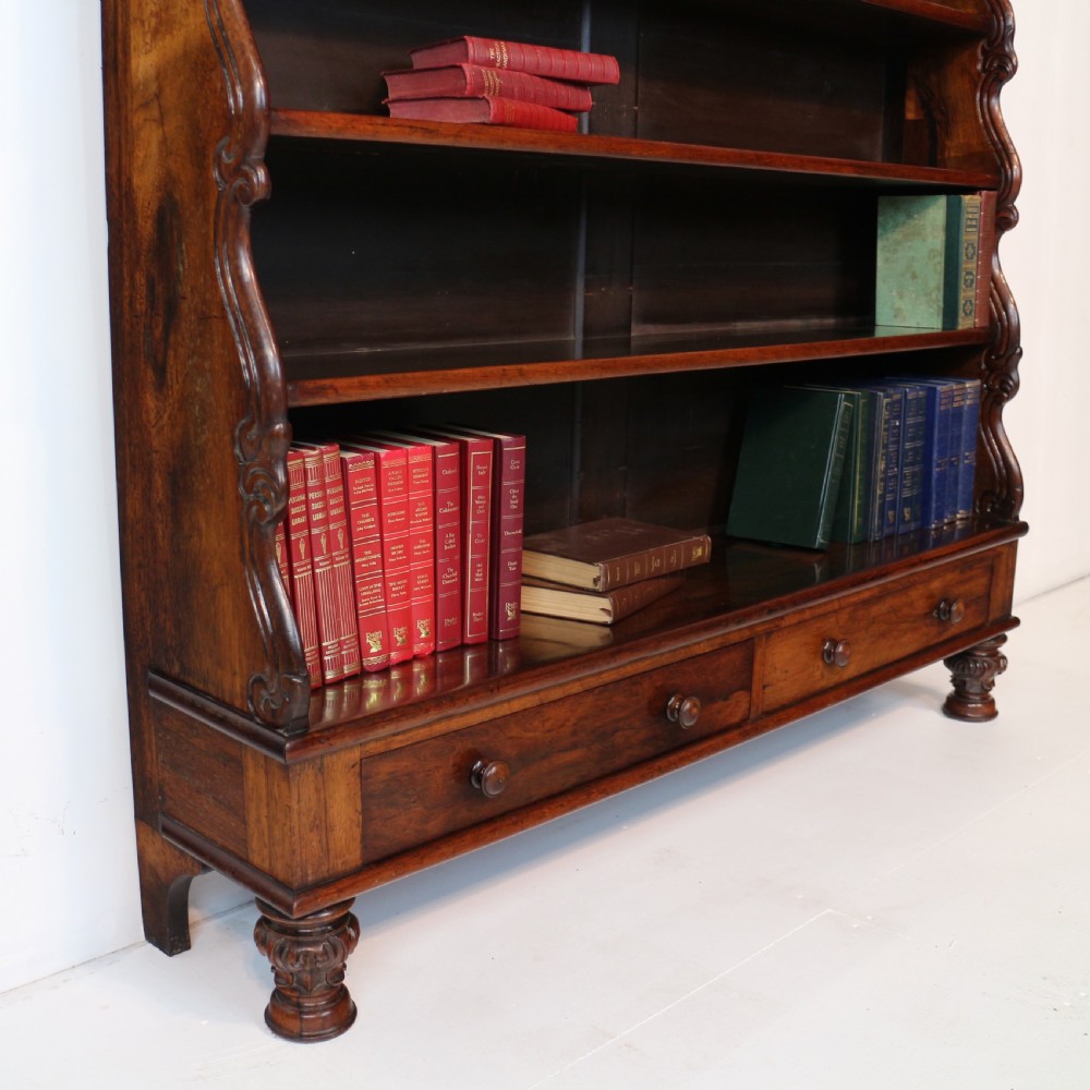 A Regency period rosewood waterfall bookcase with graduated open shelves, carved scroll sides, lower drawers, and turned feet. View XV