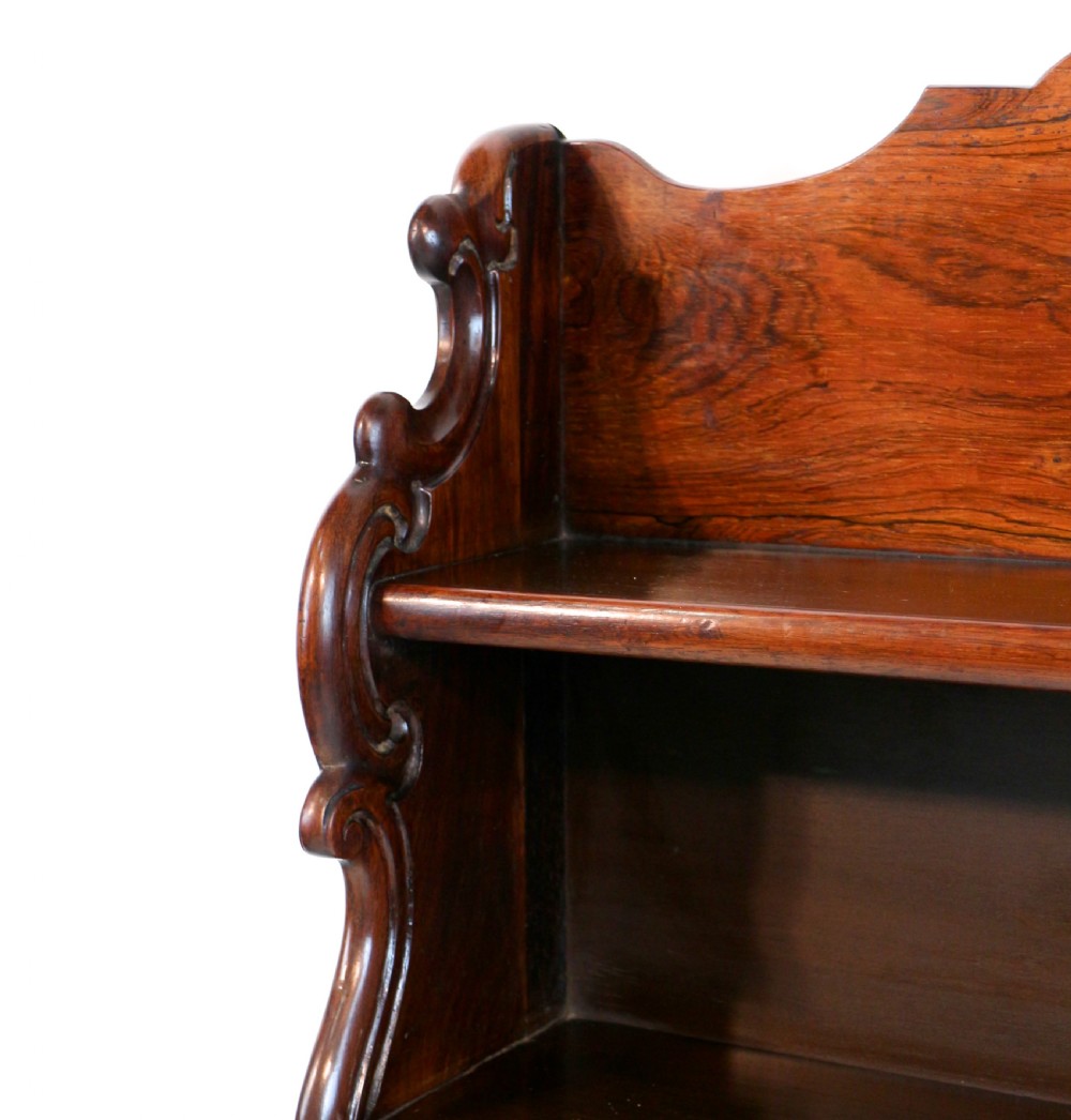 A Regency period rosewood waterfall bookcase with graduated open shelves, carved scroll sides, lower drawers, and turned feet. View XVI