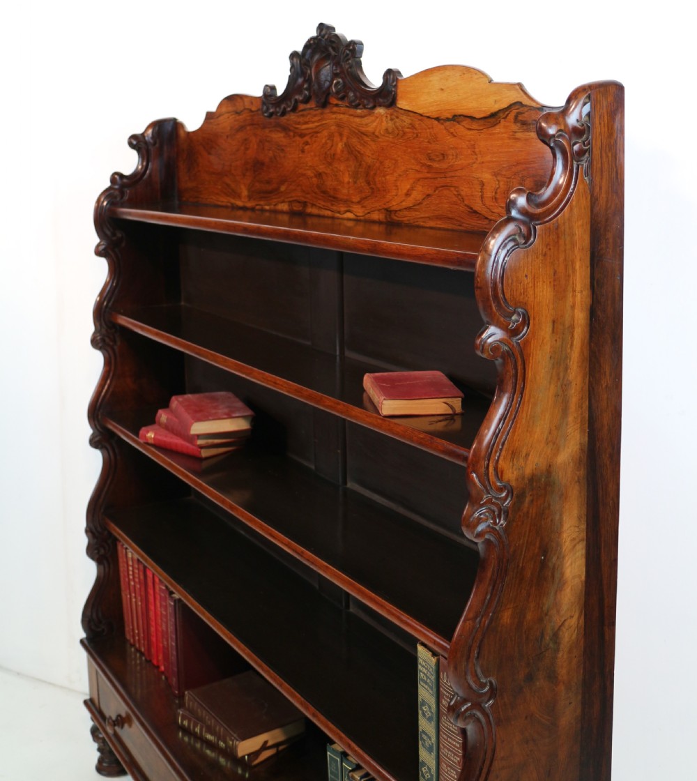 A Regency period rosewood waterfall bookcase with graduated open shelves, carved scroll sides, lower drawers, and turned feet. View XVII