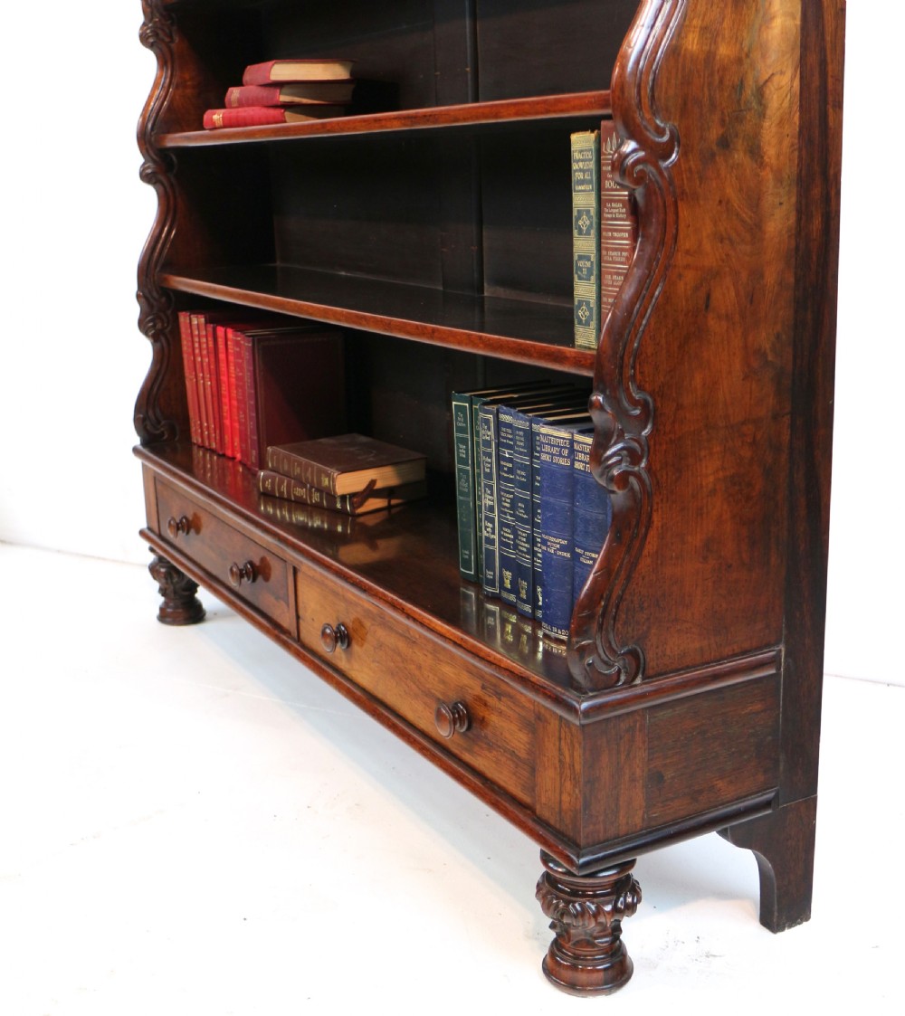 A Regency period rosewood waterfall bookcase with graduated open shelves, carved scroll sides, lower drawers, and turned feet. View XVIII