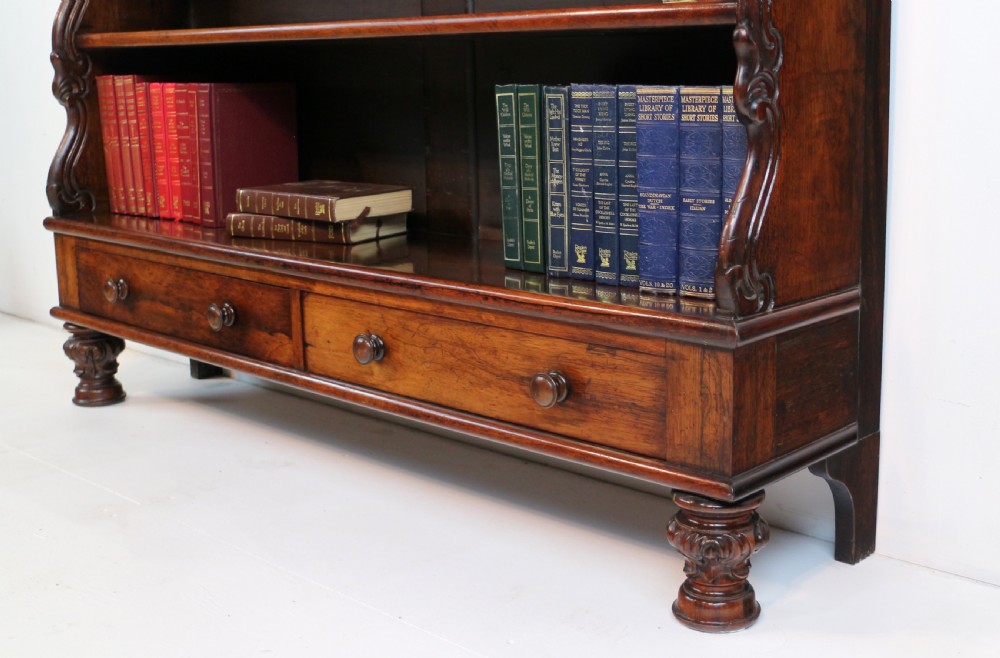 A Regency period rosewood waterfall bookcase with graduated open shelves, carved scroll sides, lower drawers, and turned feet. View XIX