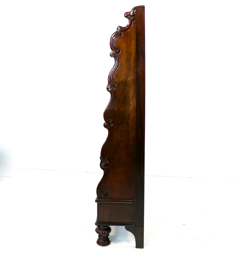 A Regency period rosewood waterfall bookcase with graduated open shelves, carved scroll sides, lower drawers, and turned feet. View XX