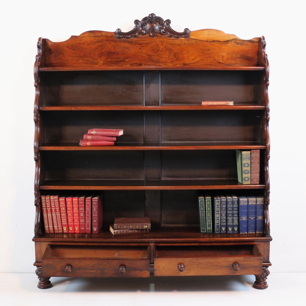A Regency period rosewood waterfall bookcase with graduated open shelves, carved scroll sides, lower drawers, and turned feet. View XXI