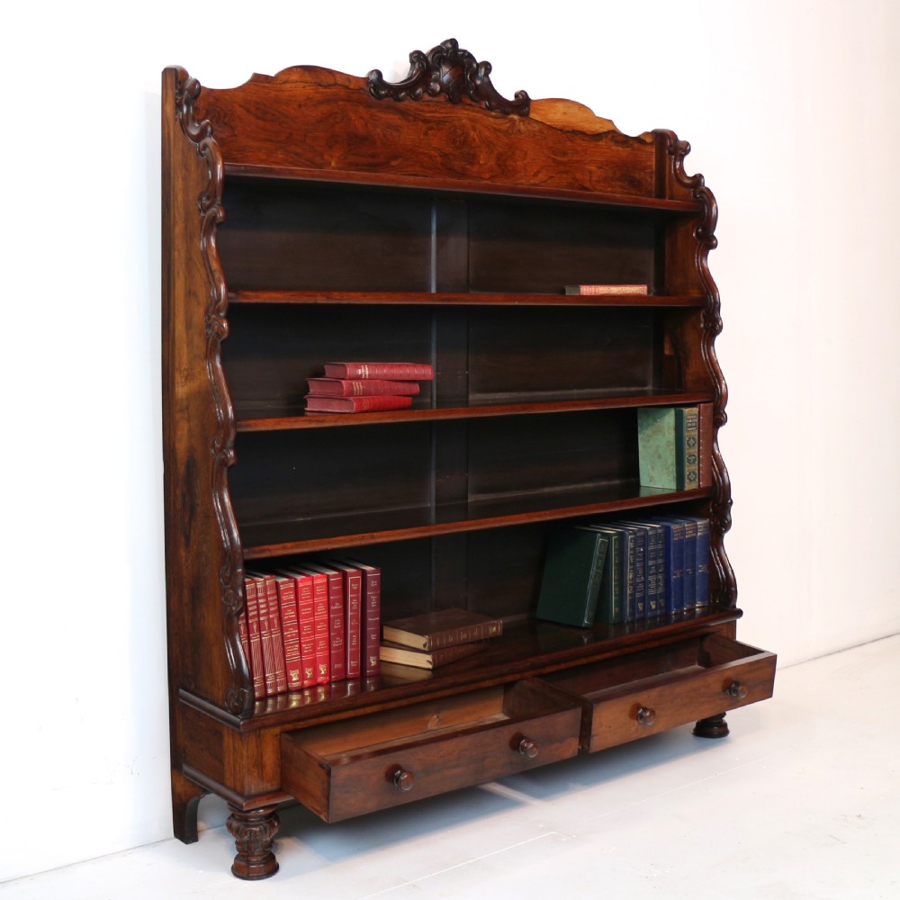 A Regency period rosewood waterfall bookcase with graduated open shelves, carved scroll sides, lower drawers, and turned feet. View XXII