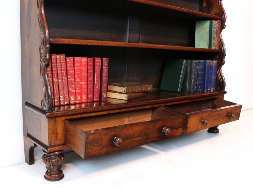 A Regency period rosewood waterfall bookcase with graduated open shelves, carved scroll sides, lower drawers, and turned feet. View XXIII