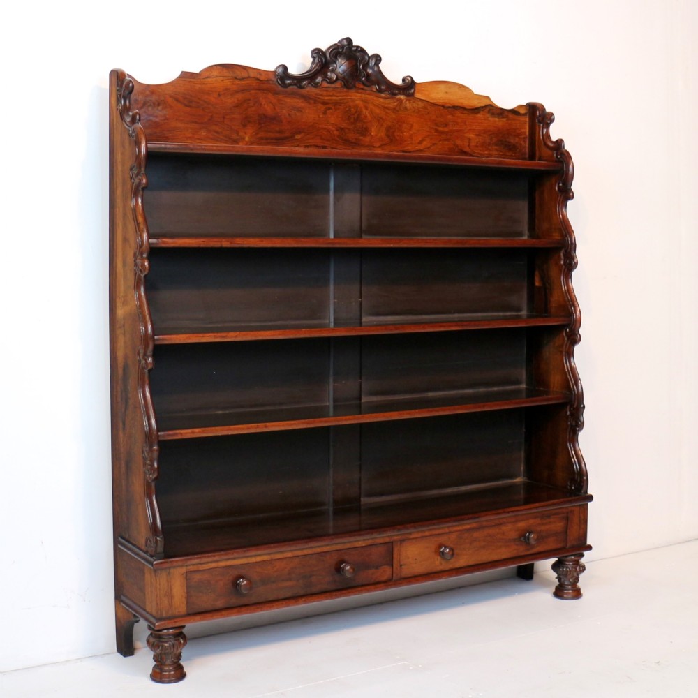 A Regency period rosewood waterfall bookcase with graduated open shelves, carved scroll sides, lower drawers, and turned feet. View XXIV