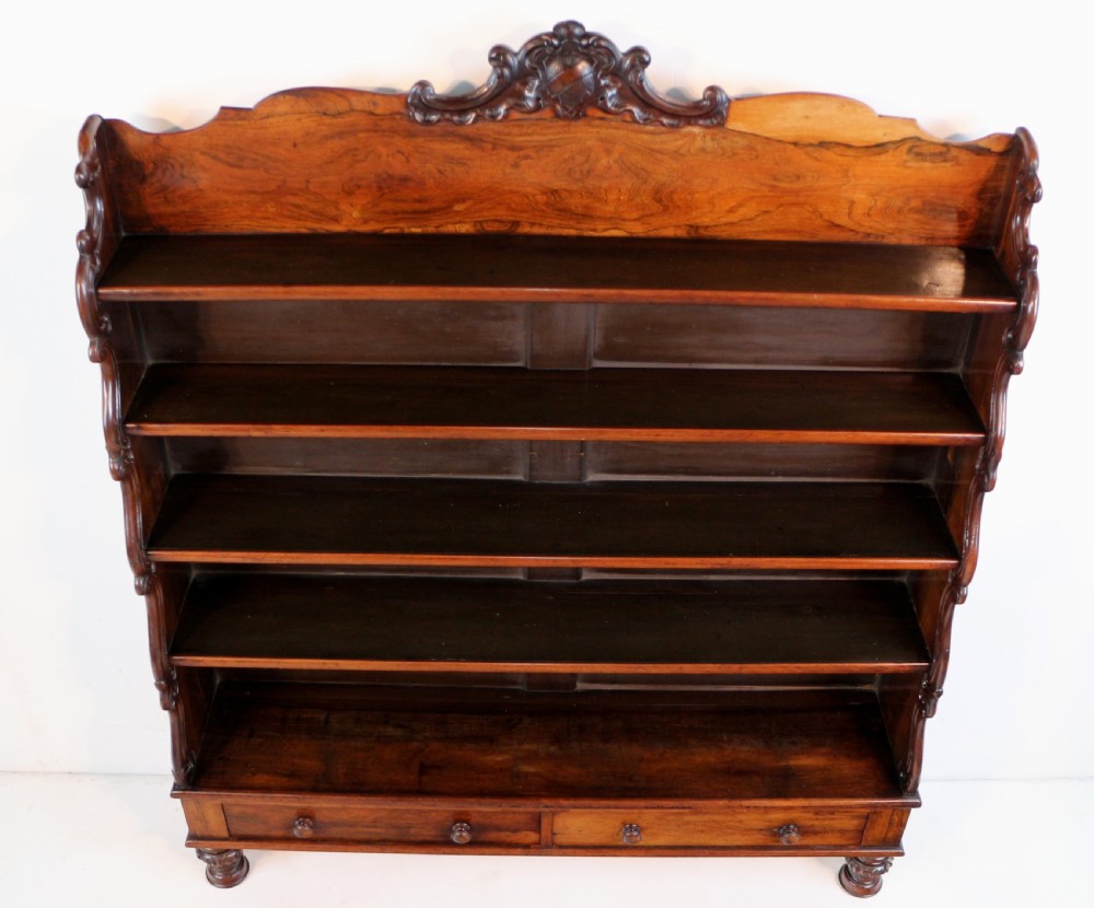 A Regency period rosewood waterfall bookcase with graduated open shelves, carved scroll sides, lower drawers, and turned feet. View XXV