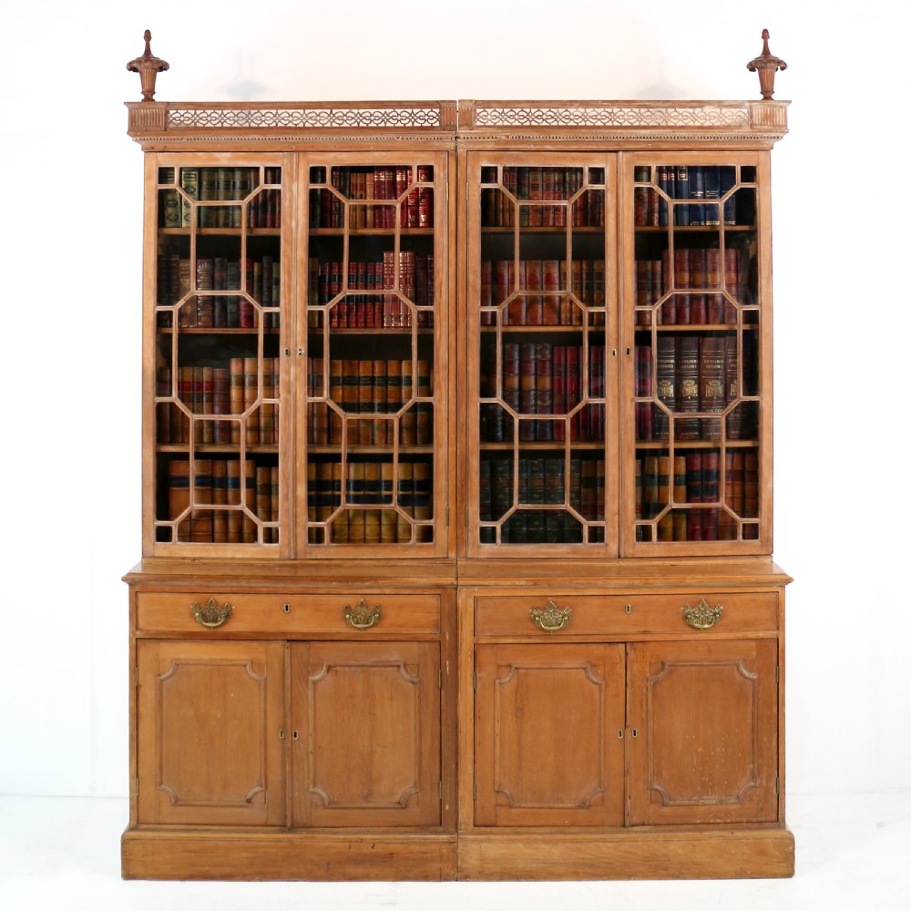 A large George III Chippendale period double bookcase crafted in natural pine, featuring astragal glazed upper doors topped with urn finials and lower panelled cupboards.