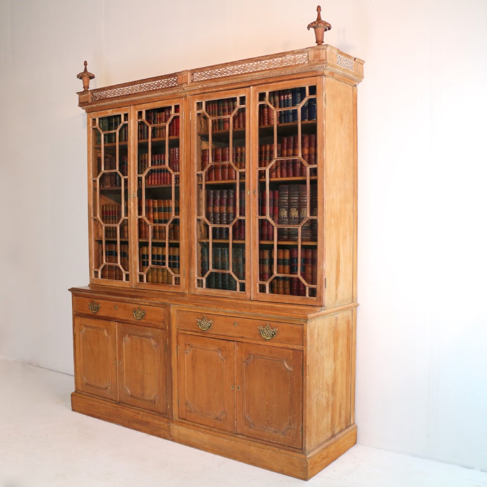 A large George III Chippendale period double bookcase crafted in natural pine, featuring astragal glazed upper doors topped with urn finials and lower panelled cupboards. View II