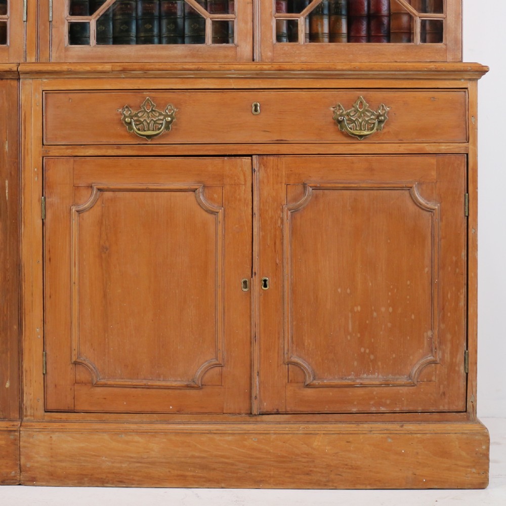 A large George III Chippendale period double bookcase crafted in natural pine, featuring astragal glazed upper doors topped with urn finials and lower panelled cupboards. View X