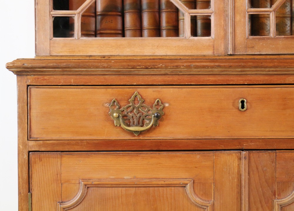 A large George III Chippendale period double bookcase crafted in natural pine, featuring astragal glazed upper doors topped with urn finials and lower panelled cupboards. View XI