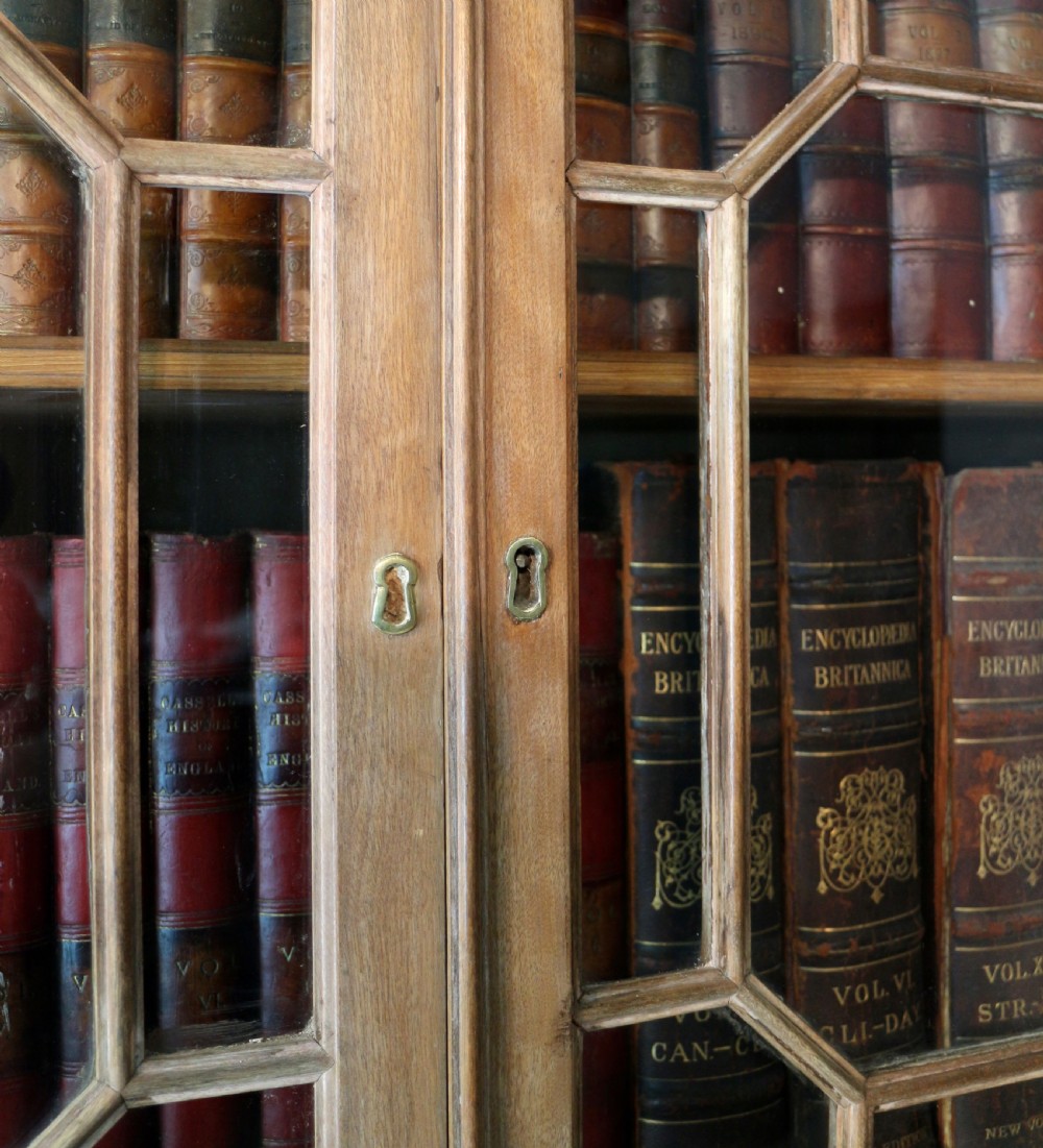 A large George III Chippendale period double bookcase crafted in natural pine, featuring astragal glazed upper doors topped with urn finials and lower panelled cupboards. View XVI