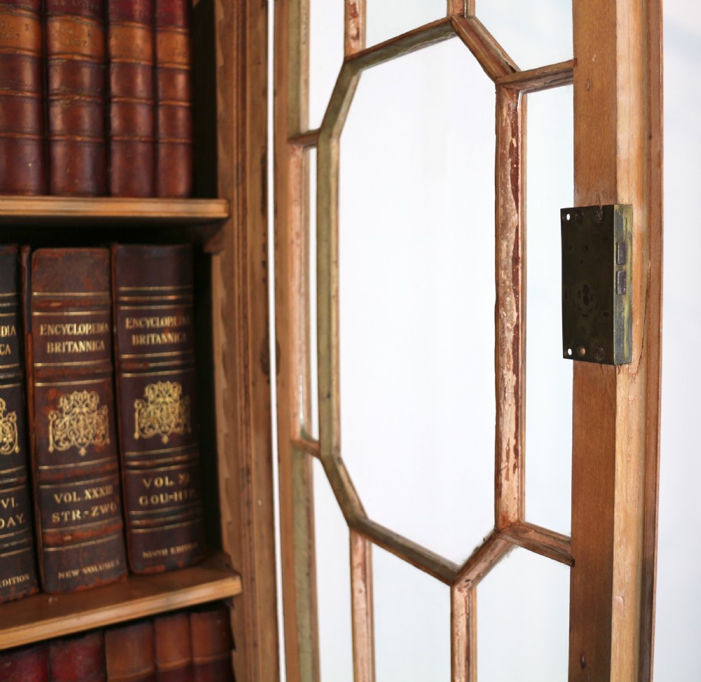 A large George III Chippendale period double bookcase crafted in natural pine, featuring astragal glazed upper doors topped with urn finials and lower panelled cupboards. View XXI